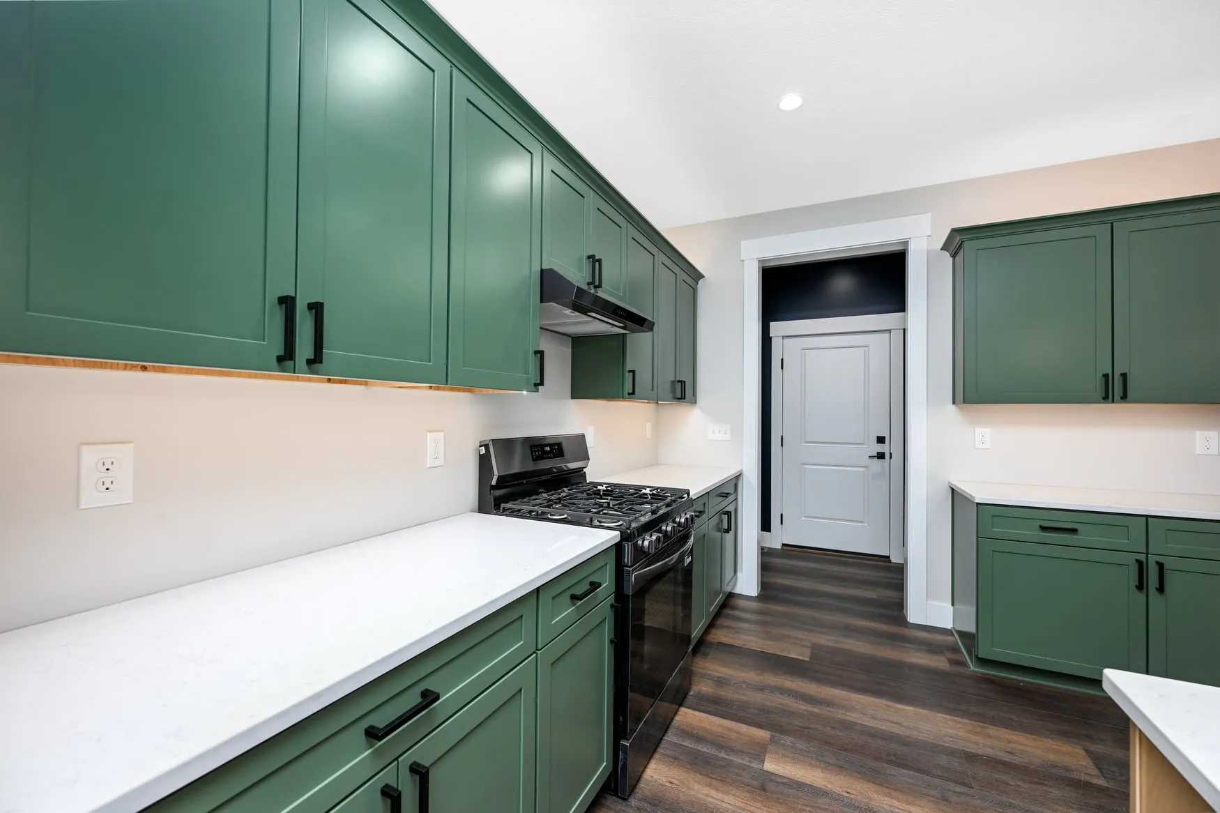 Green cabinetry with a gas range and quartz counters
